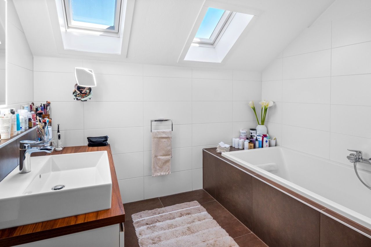 Badezimmer unter Dachfenstern mit Waschtisch aus Holz und Badewanne